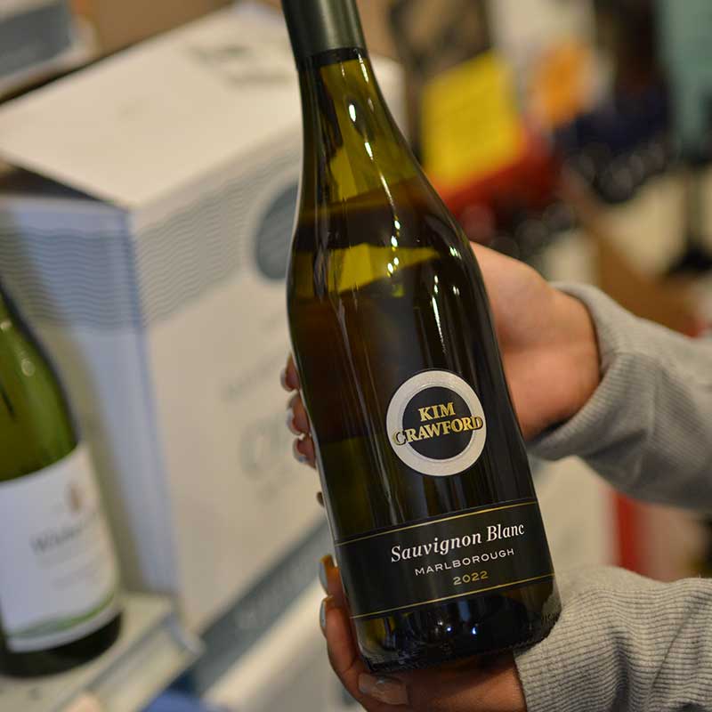 Hand holding a bottle of Sauvignon Blanc wine in front of a wine selection at Hickey's Wine & Spirits.